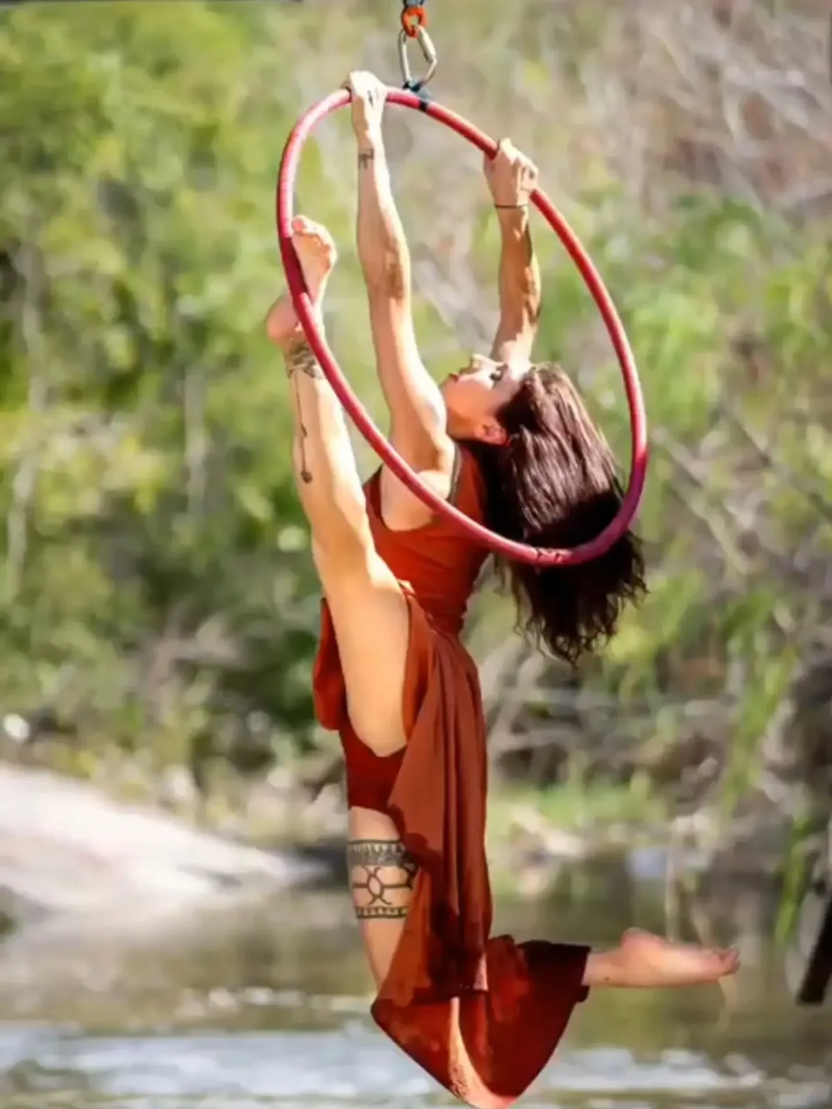 An aerialist on a lyra hoop above a river