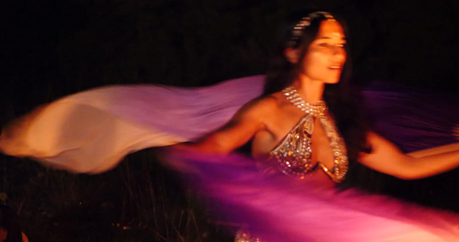 A belly dancer spins a silk veil beside a bonfire