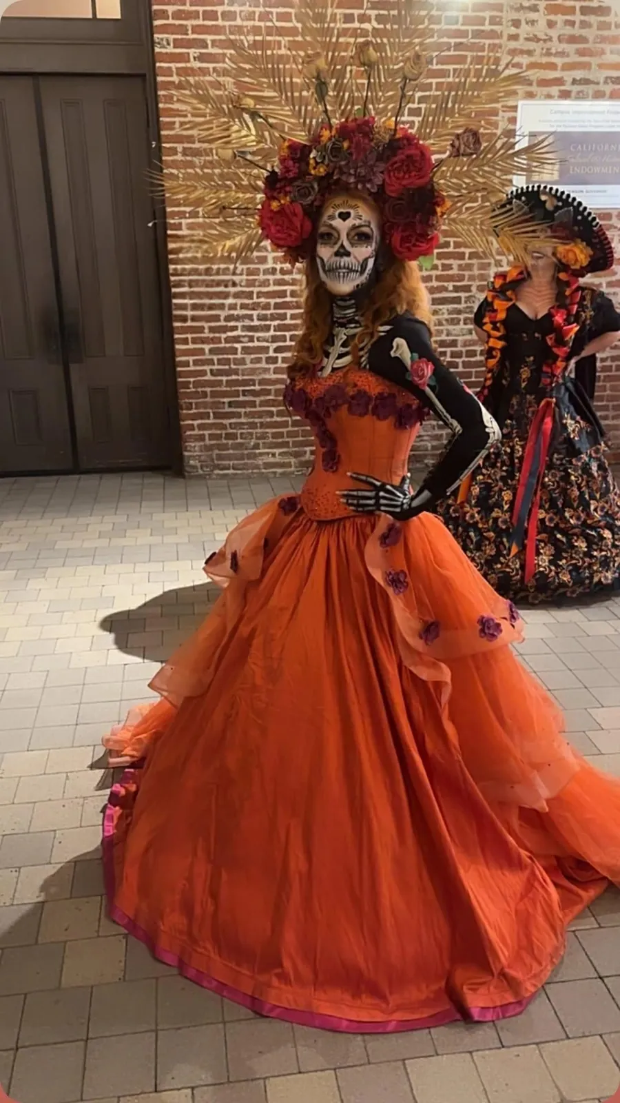A roaming performer in full Catrina costume and orange gown