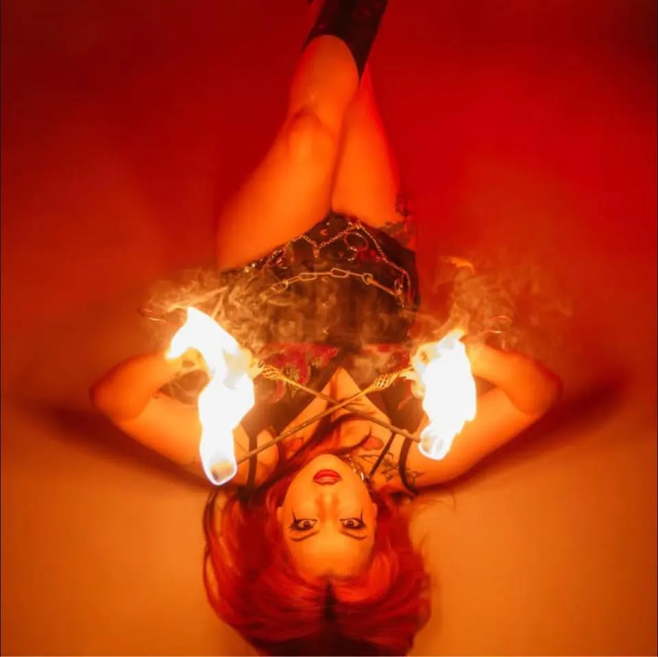An aerialist hangs upside down holding fire