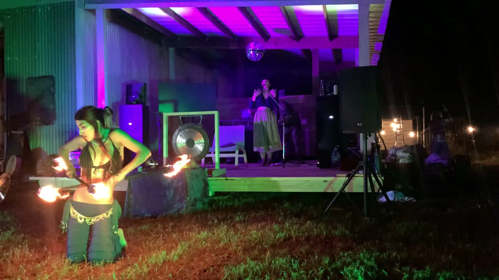 A belly dancer performs with fire in front of the outdoor stage, gong behind her