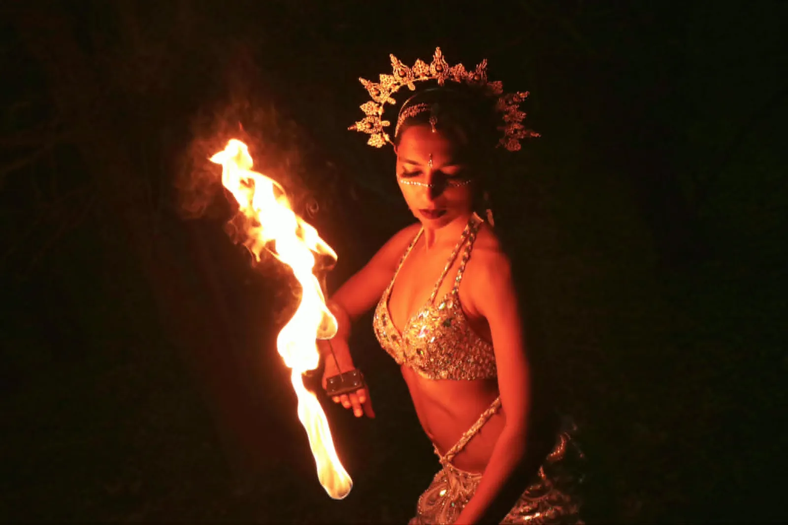 A fire dancer in a gold crown spins a flaming prop at night