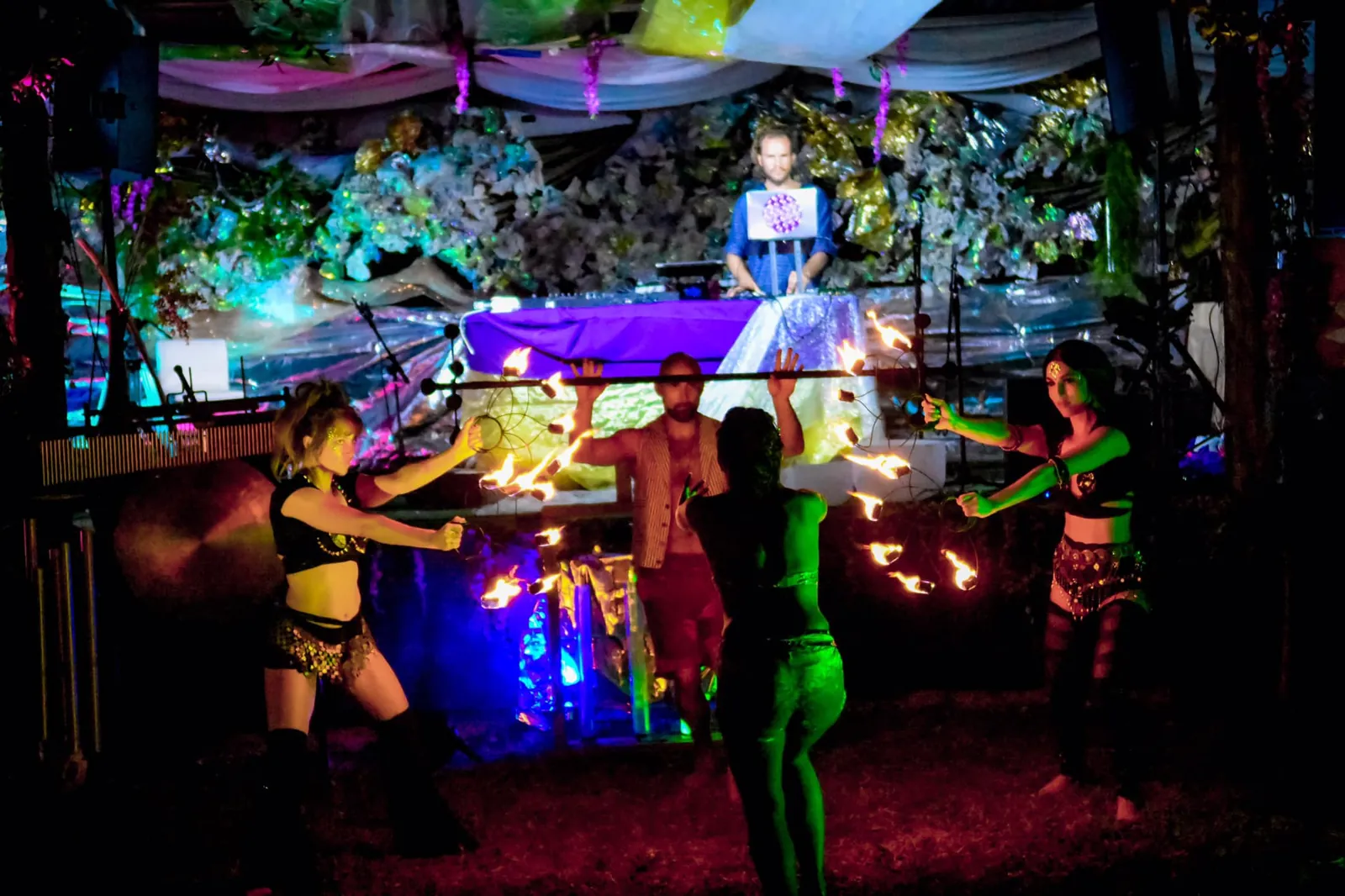 Four fire dancers spin fire in front of the DJ booth on an outdoor stage