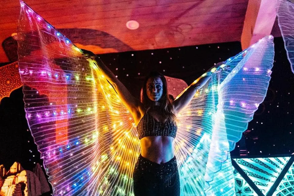 A dancer opens glowing LED wings on an indoor stage