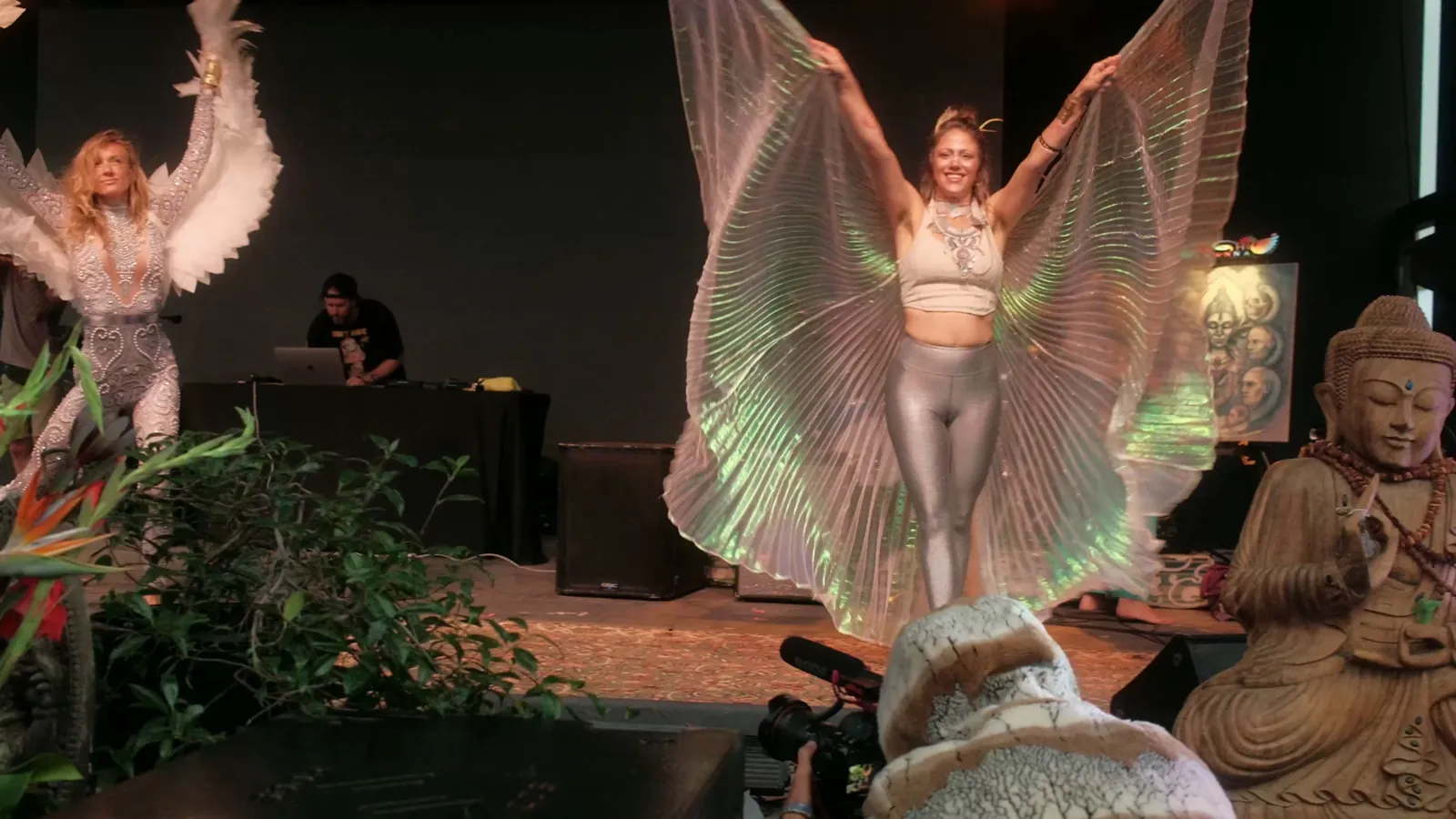 Winged dancers perform beside the DJ on a festival stage